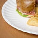 A sandwich and chips on an American Metalcraft round melamine plate on a table.