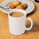 A white GET Tritan coffee mug filled with brown liquid on a wooden surface with croissants on a plate.