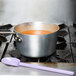 A purple Mercer Culinary high temperature mixing spoon in a pot of soup on a stove.