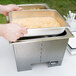 A person using Sterno Silver Vein chafing pans to prepare food on a counter in an outdoor catering setup.