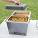 A person using a Sterno Silver Vein stackable chafer to hold food on an outdoor table.
