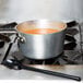 A pot of soup on a stove with a Mercer Culinary black high temperature mixing spoon in it.