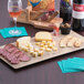 A GET faux oak wood display board with cheese, crackers, and wine on a table.