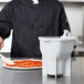 A chef using a Vollrath sauce dispenser on a pizza.