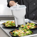 A chef using a Vollrath Traex sauce dispenser to prepare salad on a counter.