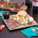 A GET faux oak wood display board with cheese, salami, and a bottle of wine on a table.