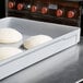 A MFG Tray dough proofing box with four white balls of dough on a counter.