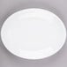 A bright white oval porcelain platter with a white rim on a gray surface.