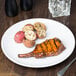 A Libbey Porcelain plate with grilled pork chops, potatoes, and silverware on a table.