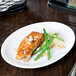 A Libbey bright white porcelain oval platter with a piece of fish and green beans on a table.