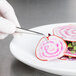 A gloved hand using Mercer Culinary curved fine point tongs to plate a beet salad.