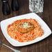 A Libbey square porcelain coupe plate with spaghetti and meatballs on a wooden table.