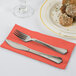 A fork and knife on a coral orange paper dinner napkin.