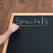 A person writing specials on a black Aarco chalk board.