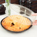 A hand using a D&W Fine Pack clear plastic dome lid to cover a black pie container holding a pie.