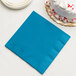 A turquoise blue Creative Converting paper dinner napkin next to a white cake.