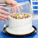 A person's hands putting a cake in a D&W Fine Pack plastic container with a clear dome lid.