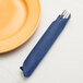 A fork and knife sitting in a navy blue Creative Converting paper dinner napkin on a table next to a plate.