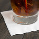 A glass of liquid on a white Creative Converting beverage napkin.