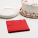 A white cake with red sprinkles next to a Classic Red beverage napkin.