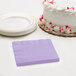 A stack of Creative Converting luscious lavender beverage napkins on a table with a cake.