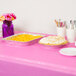 A table with a Candy Pink Creative Converting plastic table cover and trays of food on it.