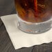 An ivory Creative Converting beverage napkin with a glass of liquid on it.