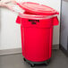 A person using a white Rubbermaid lid to open a red Rubbermaid trash can.