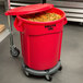 A red Rubbermaid BRUTE trash can with lid and dolly full of food.