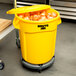 A yellow Rubbermaid BRUTE trash can with lid and dolly full of onions.