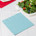 A pastel blue luncheon napkin with a fork and salad on a plate.