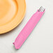 A pink Creative Converting paper napkin wrapped around silverware on a plate.