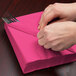 A person wrapping a Creative Converting Hot Magenta Pink luncheon napkin around a fork.