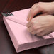 A person wrapping a Creative Converting Classic Pink luncheon napkin around a fork.
