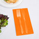 A fork and knife on a Sunkissed Orange Creative Converting guest towel next to a plate of salad.