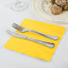 A silver fork and knife on a yellow Creative Converting 1/4 fold luncheon napkin.