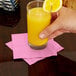 A person holding a glass of orange juice on a pink Creative Converting beverage napkin.