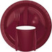 A red rectangular object with a black border and burgundy 1/4 fold luncheon napkin with silverware on a white plate.