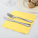 A knife and fork on a yellow napkin on a table with food