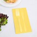 A fork and knife on a yellow napkin next to a plate of salad.