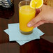 A hand holding a glass of orange juice with a Pastel Blue Creative Converting beverage napkin.