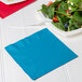 A turquoise luncheon napkin with a fork and salad on a plate.