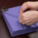 A person wrapping silverware in a purple Creative Converting luncheon napkin.