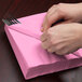 A person wrapping a candy pink Creative Converting luncheon napkin around a fork and knife.