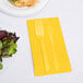 A fork and knife on a yellow Creative Converting guest towel next to a plate of salad.
