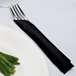 A fork and knife wrapped in a black velvet 1/4 fold luncheon napkin.