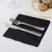 A knife and fork on a black napkin on a table with food