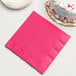 A hot magenta pink Creative Converting paper dinner napkin next to a white cake.