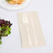 A fork and knife on an ivory Creative Converting guest towel next to a plate of salad.