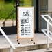 An Aarco narrow white oak A-frame sign with a white porcelain board on the steps of a building.